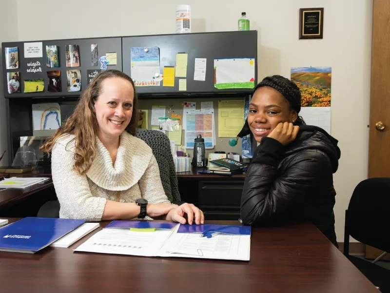 Two women sitting at a desk, looking over a folder together at Student Support.